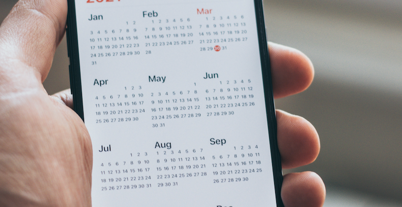 man holding iPhone with calendar application opened. 