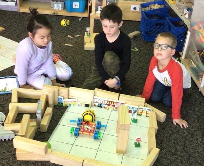 3 students code a Beebot through a block town.